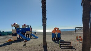 A beach playground with slides and climbing structures, palm trees, and a clear view of the ocean. - Penthouse El Carmelo New, Modernly Furnished with Huge Terrace < 50m from Beach (Caleta de Vélez)