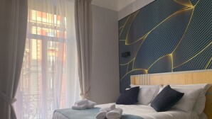 A hotel room with a bed, a headboard, a wall with a geometric pattern, and a window with curtains.