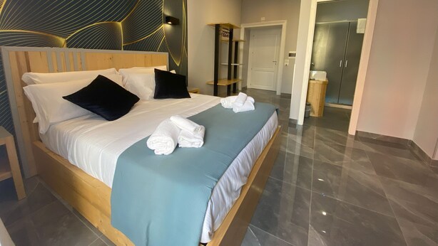 A modern hotel room with a large bed, a wooden headboard, and a decorative wall panel.