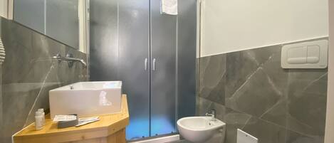 Un baño moderno con un mueble de tocador de madera, un lavabo blanco, un bidé y un inodoro.