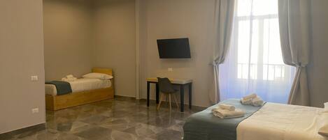 A hotel room with a bed, a desk, a chair, a television, and a window with curtains.