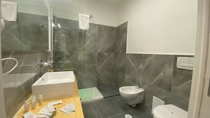 A modern bathroom with a large mirror, a sink, a bidet, and a toilet.