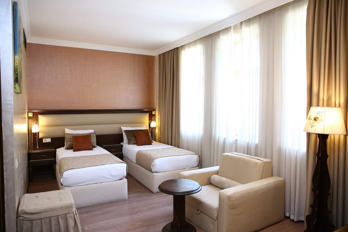 Hotellihuone, jossa on kaksi sänkyä, sohva, pieni pöytä ja lamppu.