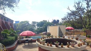 Eine Dachterrasse mit einem Rundpflanzgefäß, Sitzgelegenheiten im Freien und einem roten Sonnenschirm.