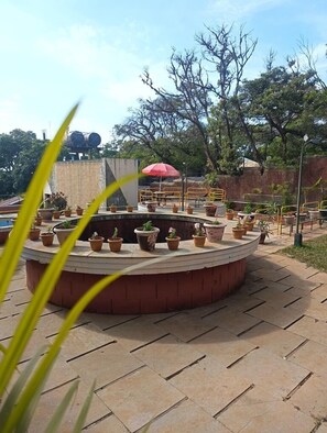 A circular outdoor seating area with potted plants and a red umbrella. - Panorama Resort Managed by Yashoda Group (Mahabaleshwar)