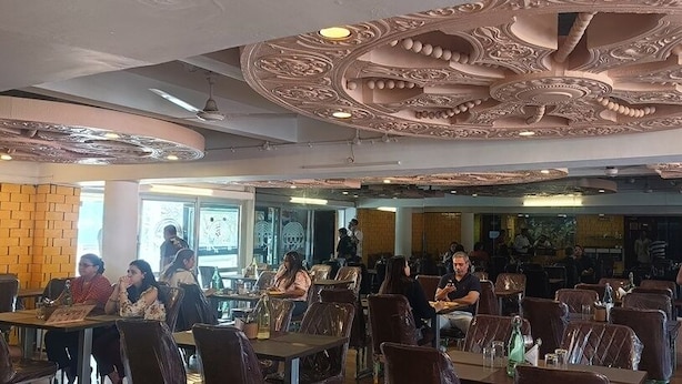 Ein Restaurant mit aufwändig gestalteten Deckenverzierungen, mehreren Esstischen und Stühlen.