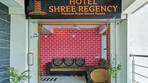 De ingang van Hotel Shree Regency, met een rode bakstenen muur en een receptie met een bank en decoratieve kussens.