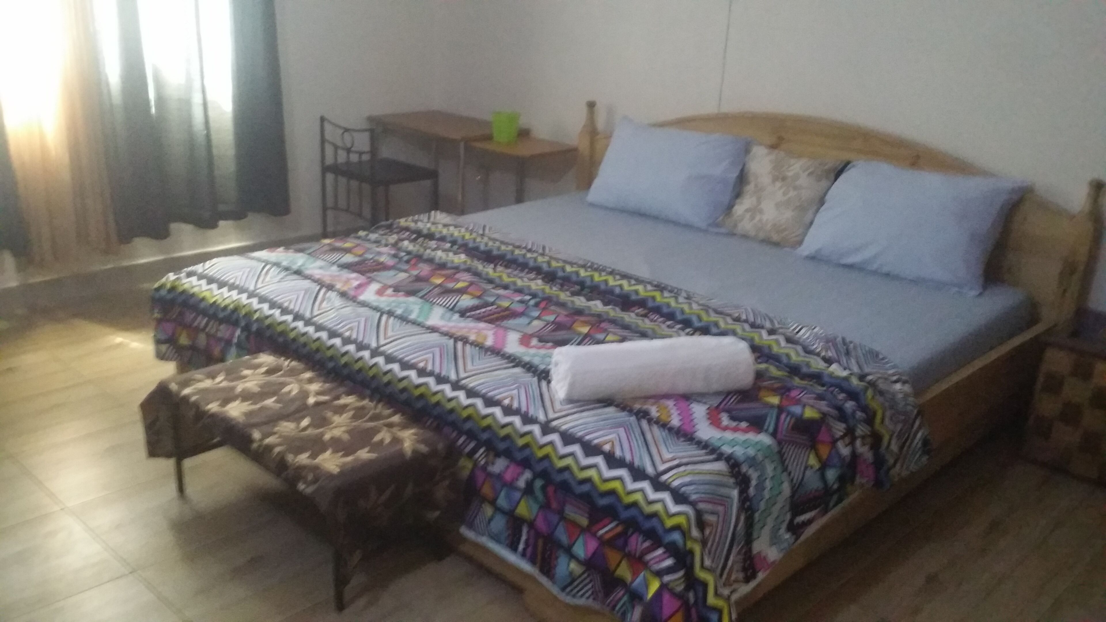 Quarto com uma cama, uma mesinha, uma cadeira e um banco.