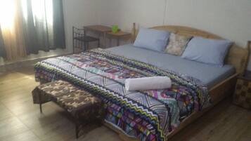 Quarto com uma cama, uma mesinha, uma cadeira e um banco.