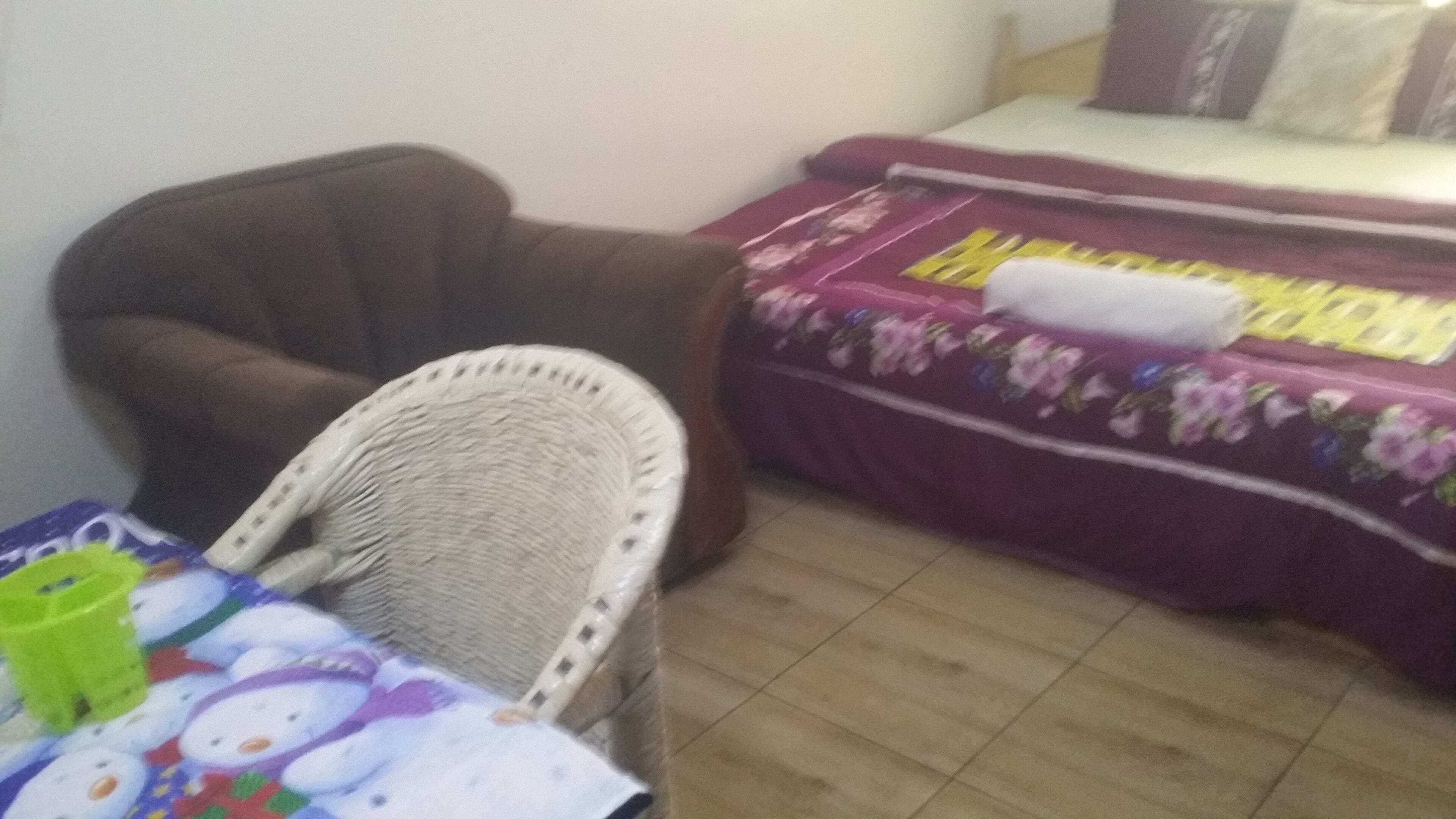 A room with a brown armchair, a small table with a Hello Kitty tablecloth, and a bed with a floral bedspread.