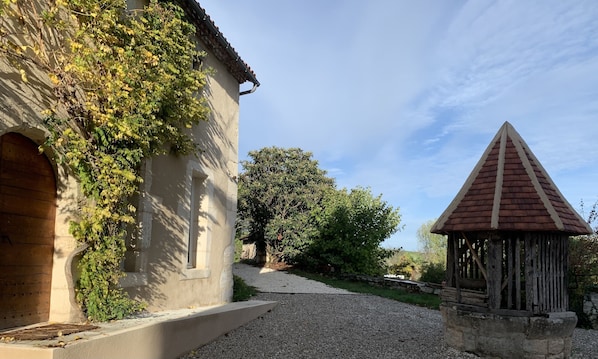 Un bâtiment doté d’une façade en pierre, d’une porte en bois et d’un chemin de gravier menant à une structure surmontée d’un toit triangulaire.