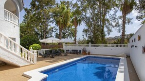 A swimming pool with a white deck, surrounded by lounge chairs and umbrellas, and a white building with a balcony. - CH Villa Golf Park La Marquesa Golf (Ciudad Quesada) (Ciudad Quesada)