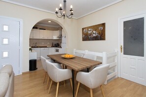 A dining area with a wooden table and white chairs, a chandelier, and a painting on the wall. - CH Villa Golf Park La Marquesa Golf (Ciudad Quesada) (Ciudad Quesada)