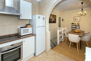 A compact kitchen with a microwave, oven, and refrigerator. There's a dining area with a wooden table and chairs.