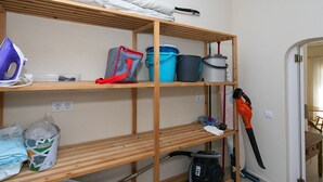 Un cuarto de almacenamiento con estantes que contienen productos de limpieza, una aspiradora y un enchufe.