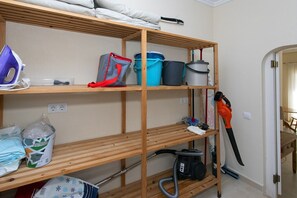 Een opslagruimte met planken vol schoonmaakmiddelen, een stofzuiger en een stopcontact.