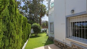 Un jardín bien cuidado con un seto recortado, un árbol pequeño y un sendero empavedado que conduce a un edificio con una ventana y una puerta.