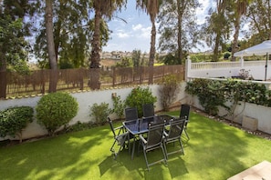Eine Terrasse mit Tisch und Stühlen, umgeben von einer weißen Mauer und viel Grün.