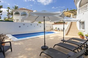 A swimming pool with lounge chairs and umbrellas, surrounded by a white building with a staircase.