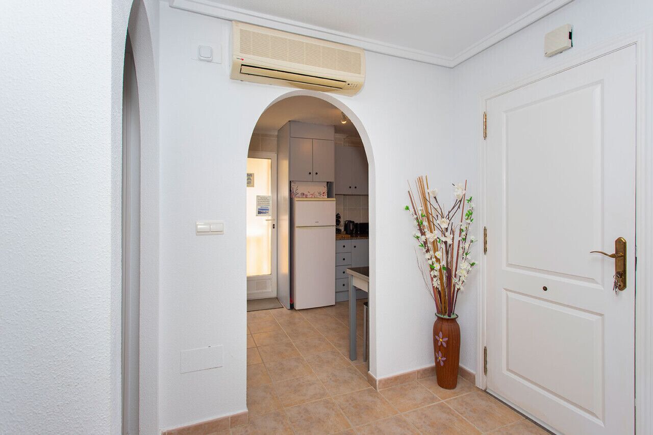 A hallway leading to a kitchen with white cabinets, a white refrigerator, and a vase with branches.