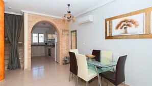 A dining area with a glass table and chairs, a kitchen in the background, and a brick archway.