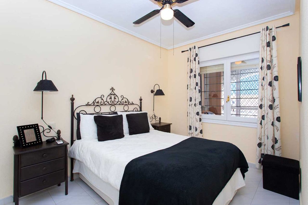 A bedroom with a bed, two bedside tables, a ceiling fan, and a window with curtains.