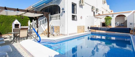 A white building with a swimming pool, outdoor seating, and a covered patio area.