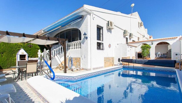 Um edifício branco com piscina, área de estar externa e varanda coberta.