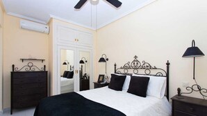 Quarto com cama, cômoda, mesa de cabeceira e luminária na parede.
