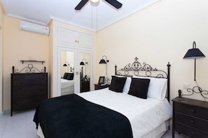 Une chambre à coucher comprenant un lit, une commode, une table de chevet et une lampe fixée au mur.
