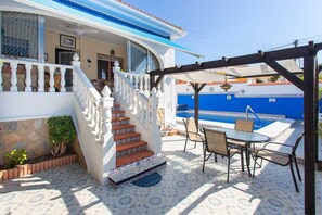 Une maison à l’extérieur blanc, agrémentée de touches de bleu, dotée d’un patio carrelé, d’un escalier et d’un coin repas avec du mobilier d’extérieur.