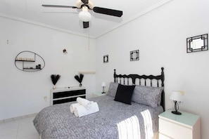 A bedroom with a bed, a ceiling fan, a bedside table with a lamp, a dresser, and a mirror on the wall.