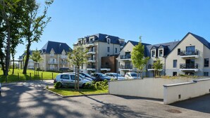 Een woongebouw met meerdere balkons, een parkeerplaats met auto's en een verzorgd gazon.