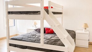 Een stapelbed met een ladder, een nachtkastje met een lamp en een raam met zonwering.
