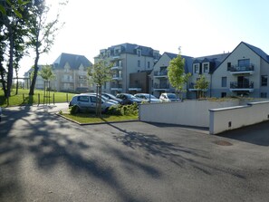 A parking area with several cars, a grassy area, and modern apartment buildings in the background. - Appartement en Résidence Entier T2 BBC à Dinard (Dinard)