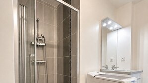 Een moderne badkamer met een douchecabine van glas, een witte wastafel en een spiegel erboven.