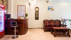 A reception area with a Coca-Cola refrigerator, a wooden reception desk, a clock, and a seating area with a wooden table and chairs.