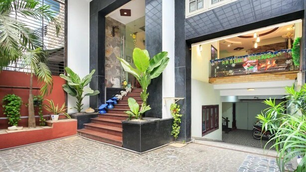 A modern building with a central staircase, surrounded by potted plants and a patterned floor.