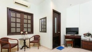 A small, well-lit room with a wooden door, a television, a desk, and two chairs.