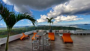 Un espace de détente extérieur moderne offrant une vue panoramique sur le paysage, notamment sur une étendue d’eau et des montagnes lointaines.