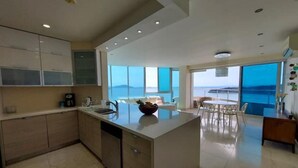 A modern kitchen with a central island, a dining area with a view, and a large window overlooking the sea. - Luxury Paradise at Playa Bonita (Panama City)