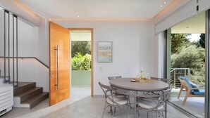 A modern interior with a dining area, staircase, and a view of greenery outside. - Kalami Beach - Villa Almyra (Kalami)