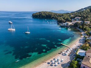 A coastal area with clear waters, boats, and a beach with umbrellas.