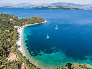 An aerial view of a coastal area with a beach, clear waters, and two sailboats.