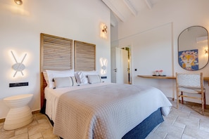 A bedroom with a bed, bedside lamps, a wooden headboard, a bedside table, a chair, and a mirror.