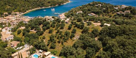 An aerial view of a coastal area with houses, a swimming pool, and boats on the water.
