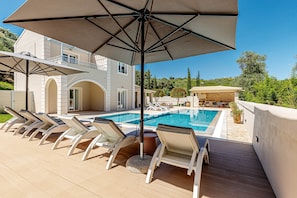 Área da piscina com espreguiçadeiras, um grande guarda-sol e piscina.