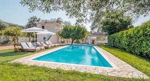 Una piscina con sillones de descanso, una pérgola y un edificio al fondo.