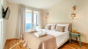 Hotellihuone, jossa on suuri sänky, pieni pöytä juomineen ja näkymä merelle.