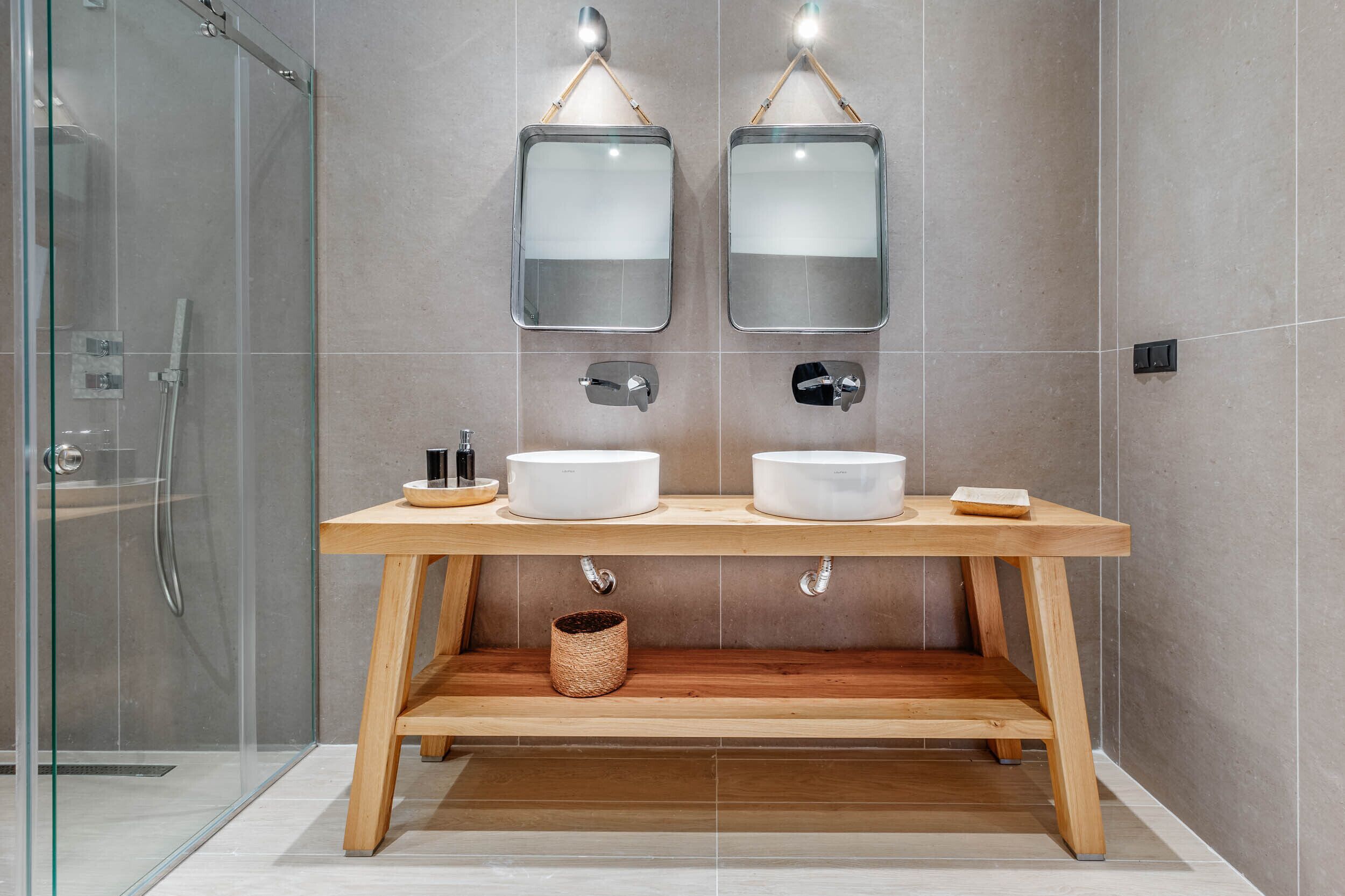 A modern bathroom with two sinks, a glass shower enclosure, and a wooden vanity.